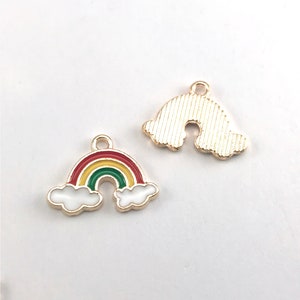 May include: Two gold-colored metal rainbow charms. One charm features a rainbow with red, yellow, and green stripes and white clouds. The other charm is a simple rainbow shape with a textured surface.