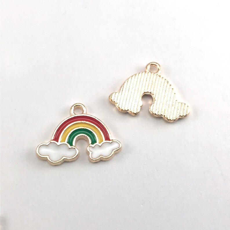 May include: Two gold-colored metal rainbow charms. One charm features a rainbow with red, yellow, and green stripes and white clouds. The other charm is a simple rainbow shape with a textured surface.