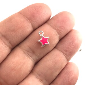 May include: A silver charm with a pink enamel star. The charm has a loop at the top for attaching to a bracelet or necklace.