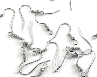 May include: A close-up of a group of silver earring hooks with a small ball at the end of each hook. The hooks are scattered on a white surface.