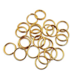 May include: A pile of 20 gold-coloured metal key rings. The key rings are all the same size and shape, and they are arranged in a random pattern.