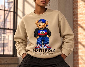 May include: A beige crewneck sweatshirt featuring a graphic of a teddy bear wearing a blue baseball cap, a gold chain, a black sweater with the Haitian flag, blue jeans, and red, white, and blue sneakers. The text reads HAITI BEAR made by The Jacques.