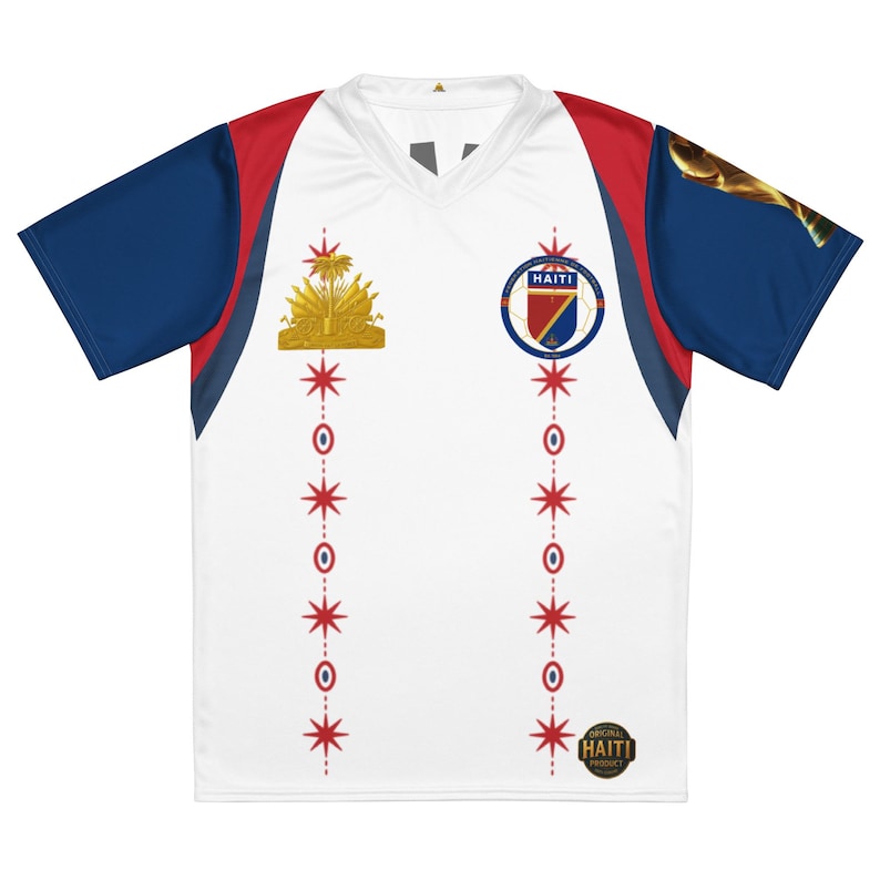 May include: A white V-neck jersey with dark blue sleeves and red accents. The front features the Haitian coat of arms, a circular Haiti soccer emblem, and two vertical rows of red star and circle icons. A gold Original Haiti Product seal is visible.