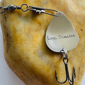 May include: A silver fishing lure with a treble hook. The lure is engraved with the words "Love, Deneice".
