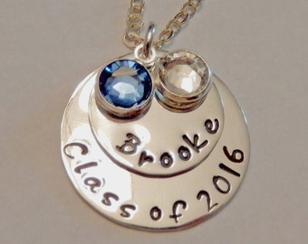 May include: Silver necklace with two round pendants. The larger pendant has the text "Class of 2016" and the smaller pendant has the text "Brooke". The necklace has a blue and clear crystal.