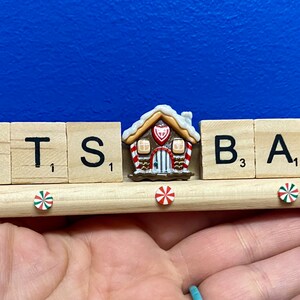 May include: A wooden sign with the words "LET'S BAKE" spelled out in Scrabble tiles. The sign is decorated with gingerbread men and a gingerbread house.