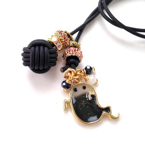 May include: A black leather cord necklace with a gold-trimmed ghost pendant. The pendant is black with glitter and has a gold outline. The necklace also features decorative beads and a black knot.