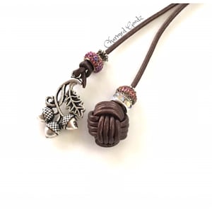 May include: Brown leather cord with a decorative knot and a silver acorn charm. The cord features a cluster of pink and purple beads and the text "Charmed Goodz". This handcrafted item is perfect for fall.