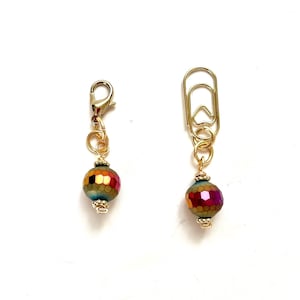 May include: Two gold-colored paperclip charms with iridescent faceted beads. One charm has a lobster clasp, the other a paperclip shape. The beads have a mix of red, orange, yellow, and teal colors.