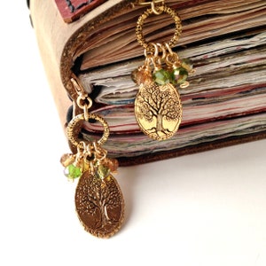 May include: A leather-bound journal with two gold tree of life charms attached to the spine. The charms are adorned with green and brown beads.