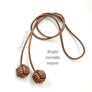 May include: Two knotted cords with bright metallic copper finish. The cords are tied together at the ends to form a loop.
