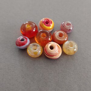 Bead lot of 9 American made lamp worked orange glass beads approximately 10 to 13mm in diameter.  Made in USA.