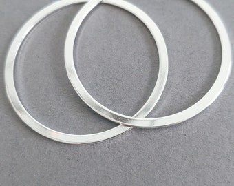 May include: Two silver hoops, one slightly larger than the other, are stacked on top of each other. The hoops are smooth and shiny.
