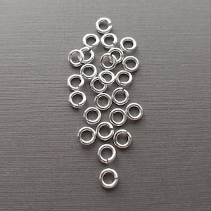May include: A pile of silver jump rings, a type of jewellery finding, on a grey background. The rings are arranged in a loose, triangular shape. The text "SNAPEEZ - Via Murano" is visible at the bottom of the image.