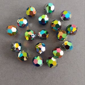 May include: A collection of iridescent green, blue, and gold glass beads. The beads are faceted and have a reflective finish.