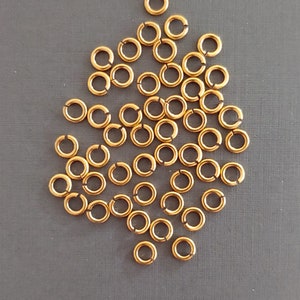 May include: A pile of 30 gold jump rings, a type of jewelry finding used for connecting chains, cords, and other jewelry components.
