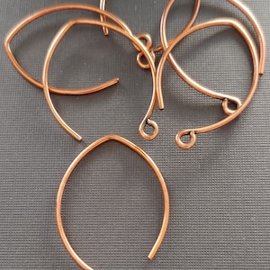 May include: Five copper wire hoops with a rounded edge and a small loop at the bottom. The hoops are arranged in a pile on a dark gray surface.
