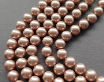 May include: A strand of round, iridescent, light brown glass beads. The beads are arranged in a curved pattern on a gray surface. The text "Via Murano" is visible at the bottom of the image.