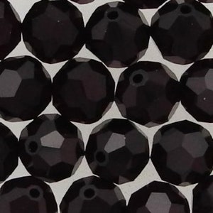 May include: A close-up of a group of dark purple faceted round beads. The beads are arranged in a random pattern and are all the same size.