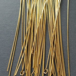 Op de afbeelding: Een stapel gouden kopspelden met een lus aan de bovenkant. De spelden zijn ongeveer 2,5 cm lang.