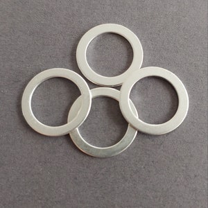 Peut inclure: Quatre anneaux en métal argenté, chacun de forme circulaire et à la finition lisse et polie. Les anneaux sont disposés en un tas lâche, un anneau chevauchant partiellement un autre.