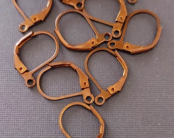 May include: A group of ten gold-toned earring hooks, also known as earring findings, are scattered on a gray textured surface. The hooks are made of metal and have a spring-loaded closure.