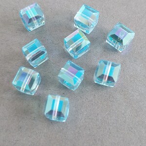May include: Ten light blue square glass beads with iridescent facets. The beads are approximately 1 cm in size.