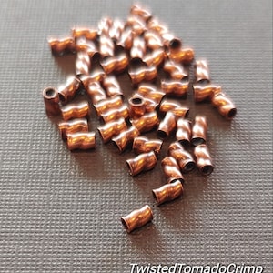 May include: A pile of copper-coloured twisted crimp beads. The beads are small and have a textured surface. TwistedTornadoCrimp is written on the surface below the beads.
