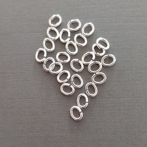 May include: A pile of silver jump rings, oval shaped, on a gray background.  SNAPEEZ - Via Murano.