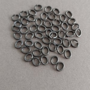 May include: A pile of 50 black metal jump rings. The rings are oval shaped and are approximately 8mm in diameter.