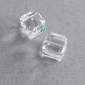 May include: Two clear glass square beads with a hole through the center. The beads are faceted and have a slight rainbow effect.