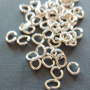 May include: A pile of silver jump rings, a type of jewelry finding used for connecting chains, cords, and other jewelry components.  The rings are small and oval-shaped, with a smooth, polished finish.  SNAPEEZ - Via Murano.