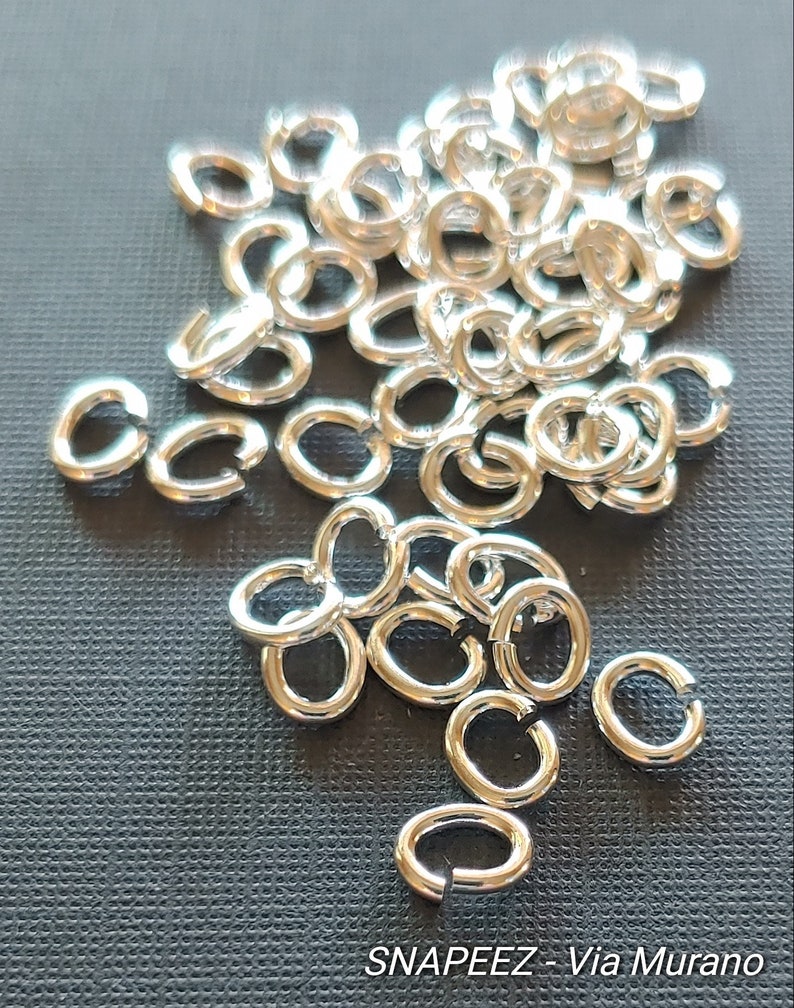 May include: A pile of silver jump rings, a type of jewelry finding used for connecting chains, cords, and other jewelry components.  The rings are small and oval-shaped, with a smooth, polished finish.  SNAPEEZ - Via Murano.