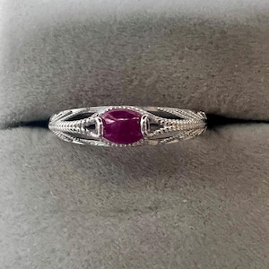 May include: A silver ring with a red gemstone set in a delicate, intricate design.