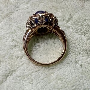 May include: A gold ring with a large blue gemstone surrounded by smaller white gemstones. The ring has a detailed, ornate design.