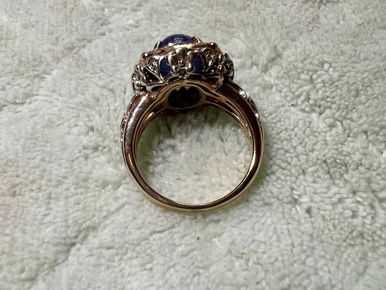 May include: A gold ring with a large blue gemstone surrounded by smaller white gemstones. The ring has a detailed, ornate design.