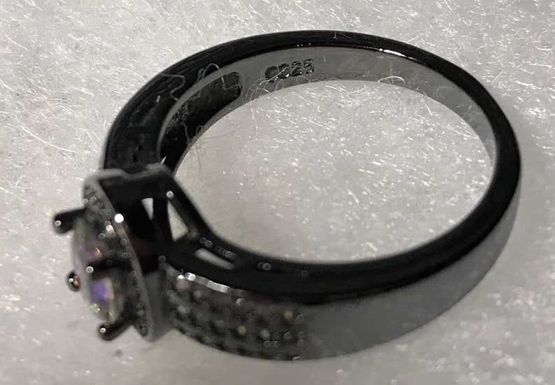 May include: Black ring with a square-shaped center stone and a band of small black stones. The ring is marked with the number "925" on the inside of the band.