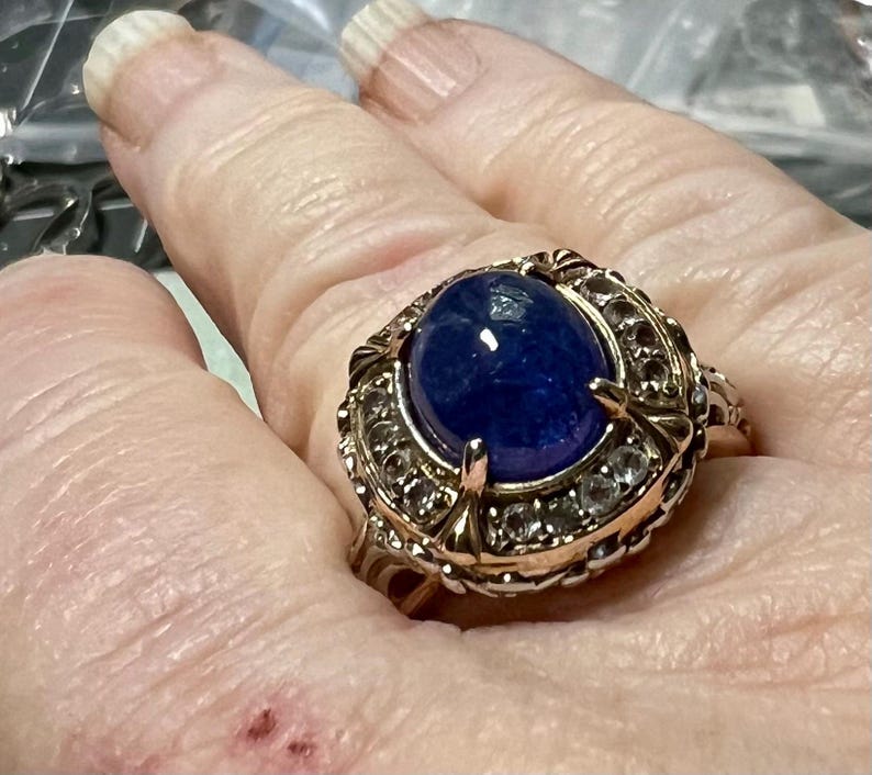 May include: A gold ring with a large oval blue gemstone surrounded by smaller clear gemstones.