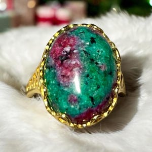 May include: A gold ring with a large oval green and pink gemstone. The gemstone has a swirling pattern of green and pink.