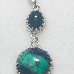 May include: A silver pendant with two round stones. The top stone is black and the bottom stone is green and black.