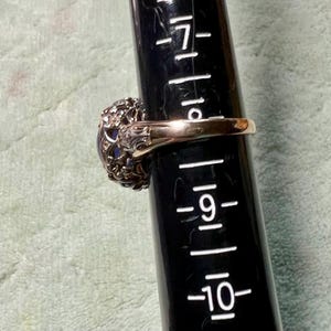 May include: A gold ring with a large, oval-shaped, dark blue gemstone surrounded by a delicate, intricate, silver filigree design.