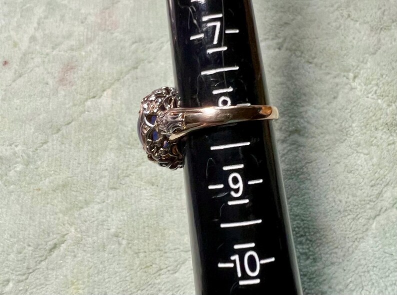 May include: A gold ring with a large, oval-shaped, dark blue gemstone surrounded by a delicate, intricate, silver filigree design.