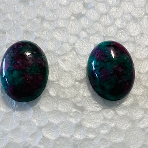 May include: A pair of oval-shaped cabochon gemstones with a green, purple, and black marbled pattern.