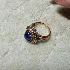 May include: A gold ring with a large blue gemstone surrounded by smaller white gemstones. The ring has a detailed, ornate design.