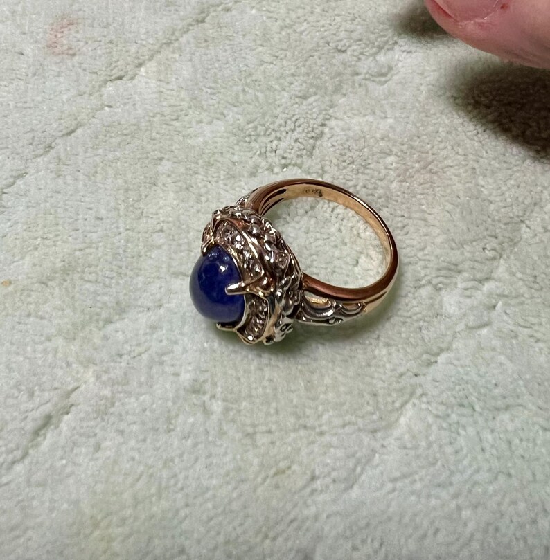 May include: A gold ring with a large blue gemstone surrounded by smaller white gemstones. The ring has a detailed, ornate design.