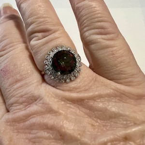 May include: A ring with a large, oval-shaped green gemstone surrounded by a halo of smaller, white gemstones. The ring is set in a silver band.