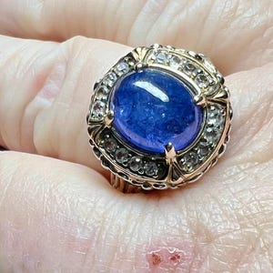 May include: A gold ring with a large blue sapphire gemstone surrounded by smaller clear gemstones.