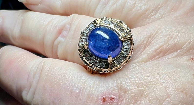 May include: A gold ring with a large blue sapphire gemstone surrounded by smaller clear gemstones.