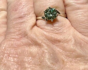 May include: A silver ring with a green gemstone set in a prong setting. The ring has a twisted band.