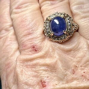 May include: A gold ring with a large blue oval gemstone surrounded by smaller clear gemstones.